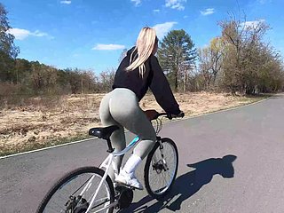 Pengendara sepeda pirang menunjukkan teman persik kepada pasangannya dan bercinta di taman umum